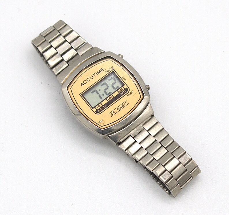 May include: A silver Accutime digital watch with a gold-toned face displaying the time 7:22. The watch has a rectangular face and a silver link band. The watch face has the words "ACCUTIME" and "QUARTZ".