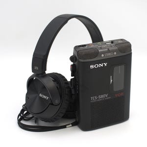 May include: Black Sony headphones and a black Sony TCS-580V stereo cassette-corder. The cassette recorder has the text "STEREO" and "V-O-R" printed on it. The headphones are connected to the recorder with a black cord.