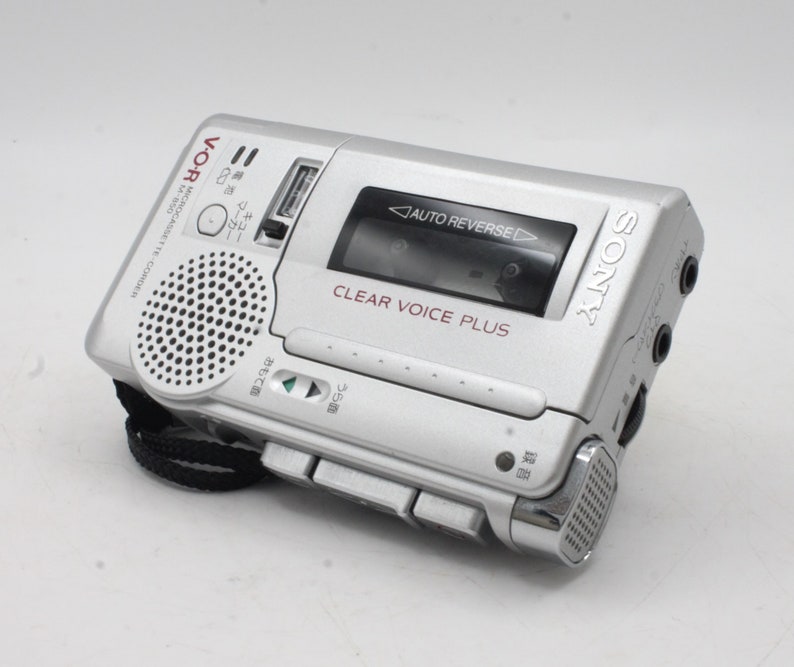 May include: A silver Sony Microcassette recorder with a black strap. The recorder has a built-in speaker, a clear voice plus feature, and auto reverse functionality. The text "V-O-R Microcassette-Corder 14-850" is printed on the side.