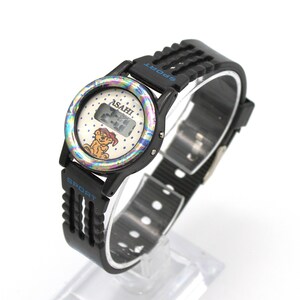 May include: Black ASAHI Sport watch with a digital display. The watch face has a colorful iridescent bezel and a cartoon bear graphic. The watch band is black with the word "SPORT" in blue.
