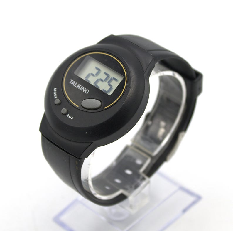 May include: Black digital talking watch with a round face. The watch displays the time 2:25 in a digital format. The watch has a black strap and features the words "TALKING", "MODE", and "ADJ".