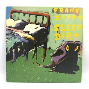 May include: Album cover for Frank Zappa's "Sleep Dirt." The artwork features a bed with a red frame, a green floor, and a black, blob-like creature with yellow eyes. The album title and artist name are in yellow text.