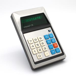 May include: Vintage Unisonic 711 calculator with a silver and black frame. The calculator displays the numbers 1 through 8 on a green screen. It has white number keys, blue function keys, and an orange percent key.