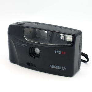 May include: A black Minolta F10BF 35mm film camera with a red eye reduction and a built-in flash.