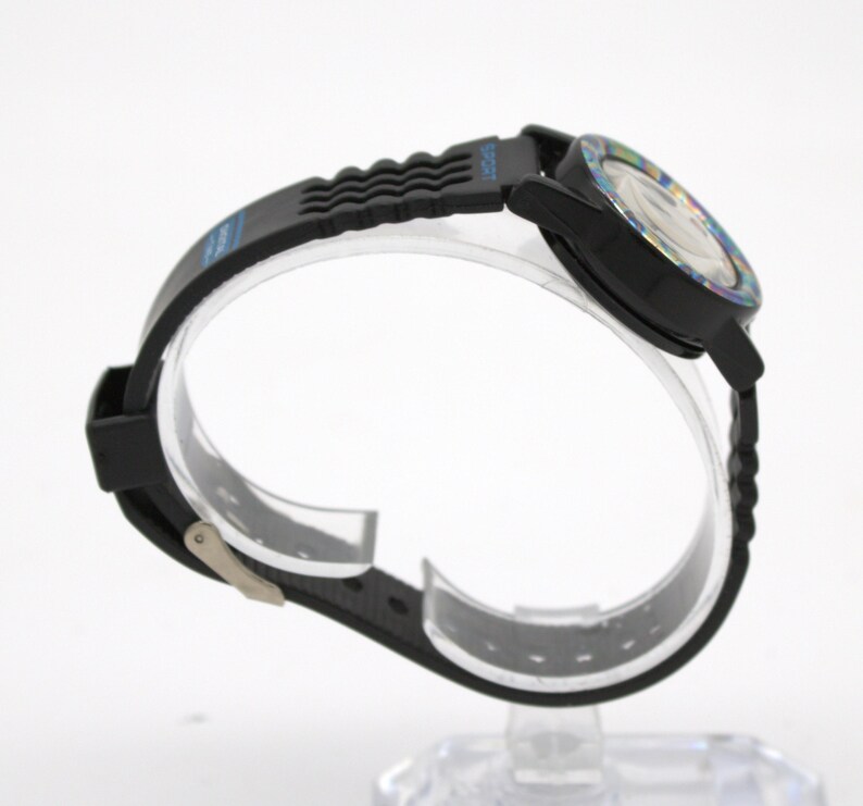May include: Black wristwatch with a black band and a colorful face. The watch has a black bezel and a black band with a wave-like design. The watch is displayed on a clear stand.