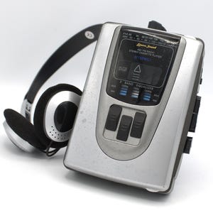 May include: A silver and black portable stereo cassette player with attached headphones. The player has a digital display and black control buttons. The headphones are black with silver accents. The text "Farave Sound" and "STEREO" are visible on the player.