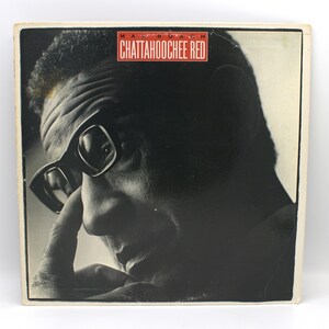 May include: Album cover featuring a black and white image of a man wearing glasses, with the title "Chattahoochee Red" in a red rectangle at the top. The album art is a close-up of the man's face.