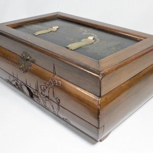 May include: A wooden jewelry box with a hinged lid and a carved design. The lid features a black background with two figures in white, and the box has a brass latch.