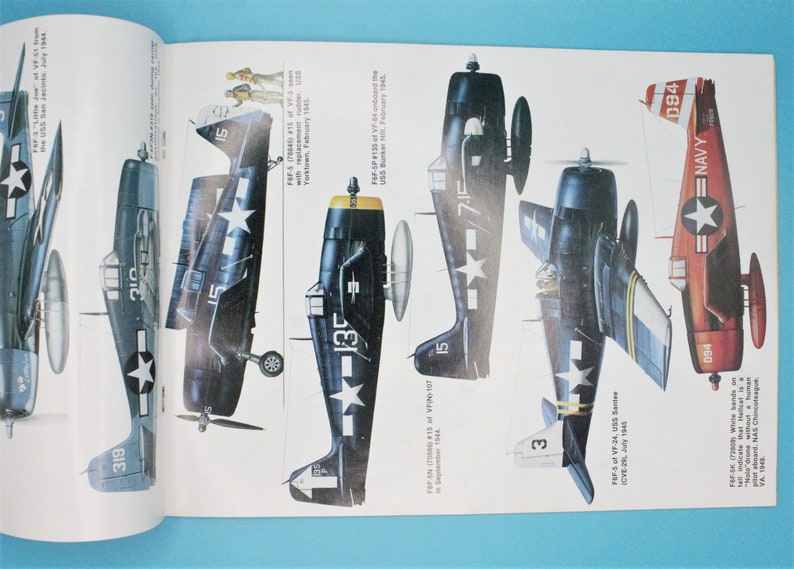 May include: A collection of five vintage aircraft illustrations, including a blue and white Grumman F6F Hellcat, a red and white Grumman F6F Hellcat, and three other blue and white Grumman F6F Hellcats. The illustrations are detailed and include markings and numbers.