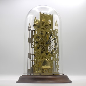 May include: A gold-toned clock in the shape of a cathedral, with a glass dome, and a wooden base.
