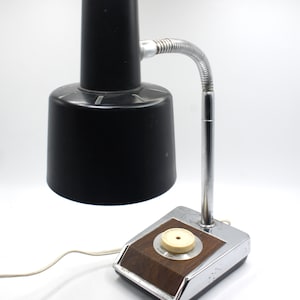 May include: A vintage black and chrome desk lamp with a flexible arm and a wooden base. The lamp has a round knob on the base with the word "Power" printed on it.