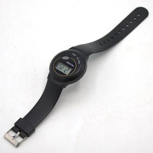 May include: Black digital talking watch with a black strap and silver buckle. The watch face displays the time, and the word "TALKING" is printed on the face. The strap is made of a flexible material.