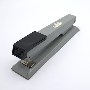 May include: A gray Bates 550 stapler with a black rubber grip. The stapler has the text "Con Edison" printed on the side. The stapler is on a white background.