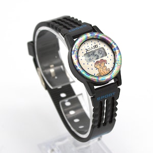 May include: Black digital watch with a black band. The watch face has a cartoon dog illustration and the word "ASAHI". The watch band has the word "SPORT" printed on it.