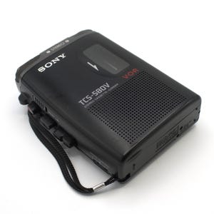 May include: Black Sony TCS-580V stereo cassette recorder with a black wrist strap. The recorder has the word "SONY" printed in white on the top left corner. The model number "TCS-580V" is printed in white on the front of the recorder.