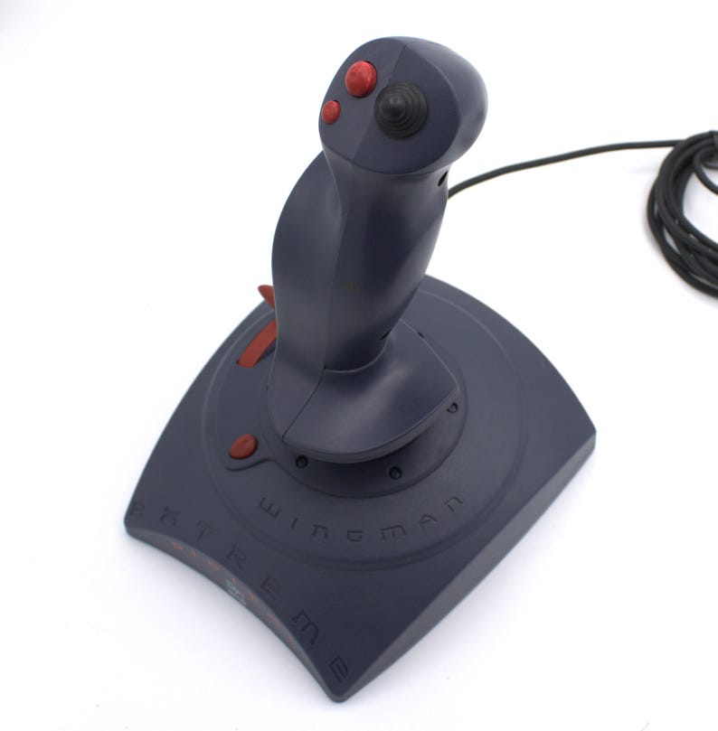 Puede incluir: Un joystick gris oscuro con botones y detalles en rojo. La base est&aacute; etiquetada como "Wingman Extreme". El joystick tiene un mango curvo y un cable negro. El dise&ntilde;o es para juegos.