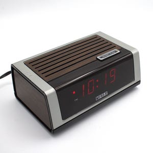 May include: A vintage Cosmo digital alarm clock with a wood grain top and sides, a black face, and a silver trim. The red LED display shows the time as 10:19 PM. The clock has a "Snooze Alarm" button.