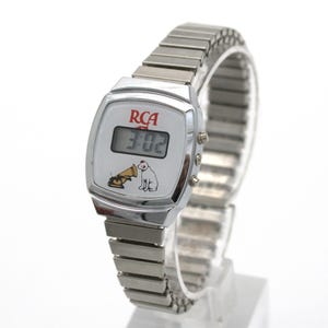 May include: A silver-tone digital wristwatch with an expandable metal link band. The white watch face features the red RCA logo, a digital time display, and a graphic illustration of a dog sitting next to a gramophone horn.