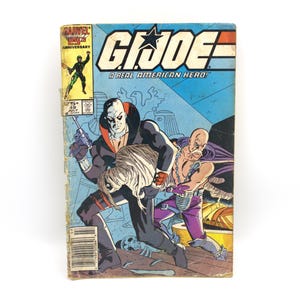 May include: A vintage G.I. Joe comic book with a blue cover featuring action-packed illustrations. The cover displays the title "G.I. Joe: A Real American Hero!" and a scene with costumed characters. The comic is marked with the Marvel 25th Anniversary logo.
