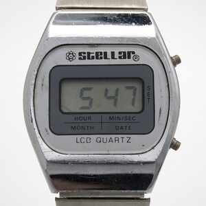 May include: A silver-toned digital wristwatch with a metallic band. The watch face features the brand name Stellar with an atom icon, a digital display showing 5:47, and the text HOUR, MIN/SEC, MONTH, DATE, and LCD QUARTZ printed on the screen.