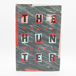 May include: A book cover with a black background and a white, red, and blue pattern. The title "THE HUNTER" is written in large, bold, black letters with a red and white background. The author's name, "ROGER BUSBY", is written in smaller, black letters with a white background.