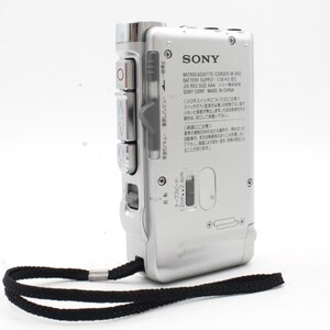 May include: A silver Sony Microcassette-Corder M-850 with a black strap. The device has a tape speed selector, play, rewind, and fast forward buttons. The text on the device reads "MICROCASSETTE-CORDER M-850 BATTERY SUPPLY 1.5Vx2 IEC, JIS R03 SIZE AAA SONY CORP MADE IN CHINA".