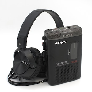 May include: A black Sony TCS-580V stereo cassette-corder with a pair of black Sony headphones. The cassette recorder has the Sony logo and the words "STEREO" and "V.O.R." printed on it. The headphones are connected to the recorder.