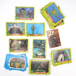 May include: A collection of Teenage Mutant Ninja Turtles trading cards featuring various characters and scenes from the cartoon series. The cards are yellow with green borders and feature images of the turtles, the Shredder, and other characters. The text on the cards includes phrases like "Let's Rock 'n' Roll!" and "Ready for Action!"