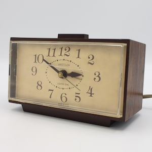 May include: A brown and gold Westclox alarm clock with a lighted dial. The clock face has black numbers and hands. The clock is made in the USA.