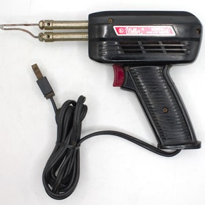 May include: A black Weller soldering iron with a red trigger and a black power cord. The soldering iron has a built-in stand and a tip for soldering.