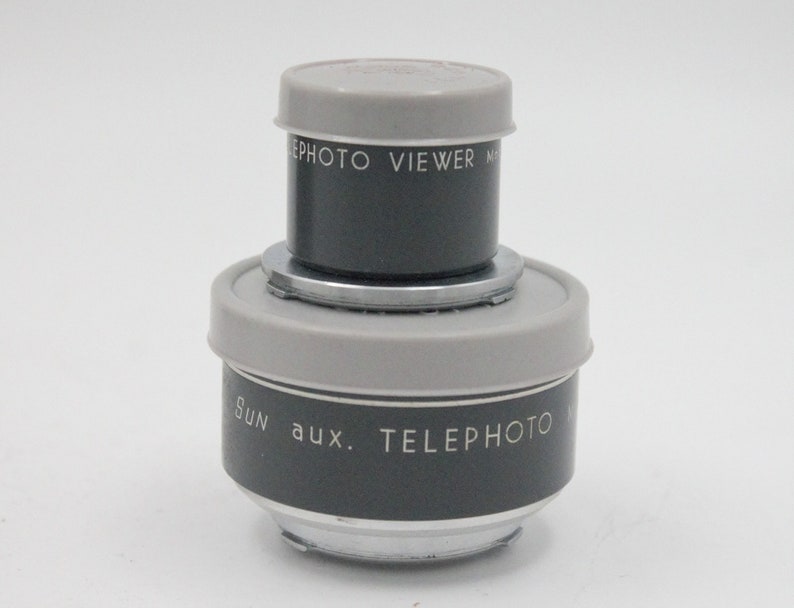 May include: A gray and silver Sun aux. Telephoto lens with a gray and silver Sun Photo Viewer lens attached to the top.