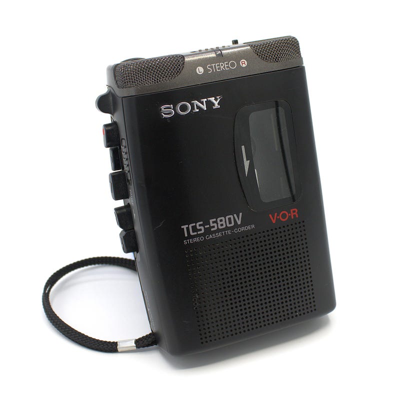 May include: Black Sony TCS-580V stereo cassette-corder with a built-in microphone and speaker. The device has a black wrist strap and the text "SONY" is visible on the front. The model number and "V-O-R" are also printed on the front.