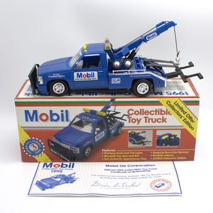 May include: A blue Mobil tow truck toy with a working head, tail lights, and movable tow arm. The toy truck is on top of a box that says "Collectible Toy Truck" and "Limited Collectors' Edition". A certificate of authenticity is also included.