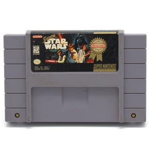 May include: A gray Super Nintendo cartridge for the game "Super Star Wars." The label features the game's title, characters, and the Nintendo logo. The cartridge is marked "SNS-V4-USA-1 MADE IN JAPAN."