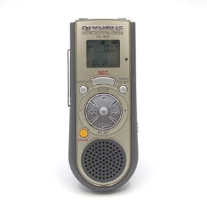 May include: A silver Olympus VN-1800 digital voice recorder with a black display screen, buttons, and a circular control knob. The screen displays "HO 000" and "10.2". The buttons include "REC", "STOP", "MENU/FOLDER", "DISPLAY", "PLAY", and "ERASE".