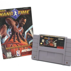 May include: A gray Super Nintendo game cartridge and instruction booklet for "NBA Hang Time." The booklet features a basketball player reaching for a basketball. The game cartridge has a label with the game title and a basketball scene.