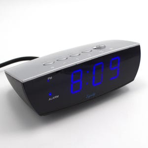 May include: A black and silver digital alarm clock displaying the time 8:09 in bright blue digits. The clock has several buttons on top and the word "Alarm" is visible. The brand name "Equity" is also visible.