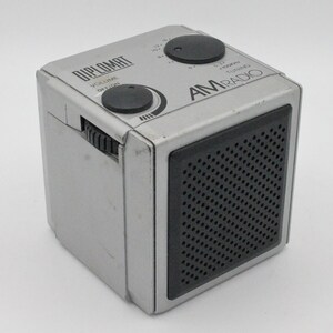 May include: A silver AM radio with a black speaker grille and the word "DIPLOMAT" printed on the side. The radio has a volume knob, a tuning knob, and an on/off switch.