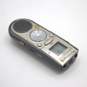 May include: A silver Olympus VN-1800 digital voice recorder with a black screen and buttons. The recorder has a built-in microphone and a headphone jack.