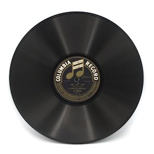 May include: A vintage black vinyl record with a gold and black label. The label reads "Columbia Record" and features musical notes. The record is a circular shape and is set against a white background.