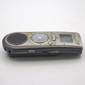 May include: A silver and black Olympus digital voice recorder with a built-in microphone, a small LCD screen, and buttons for play, stop, rec, menu, folder, and volume.