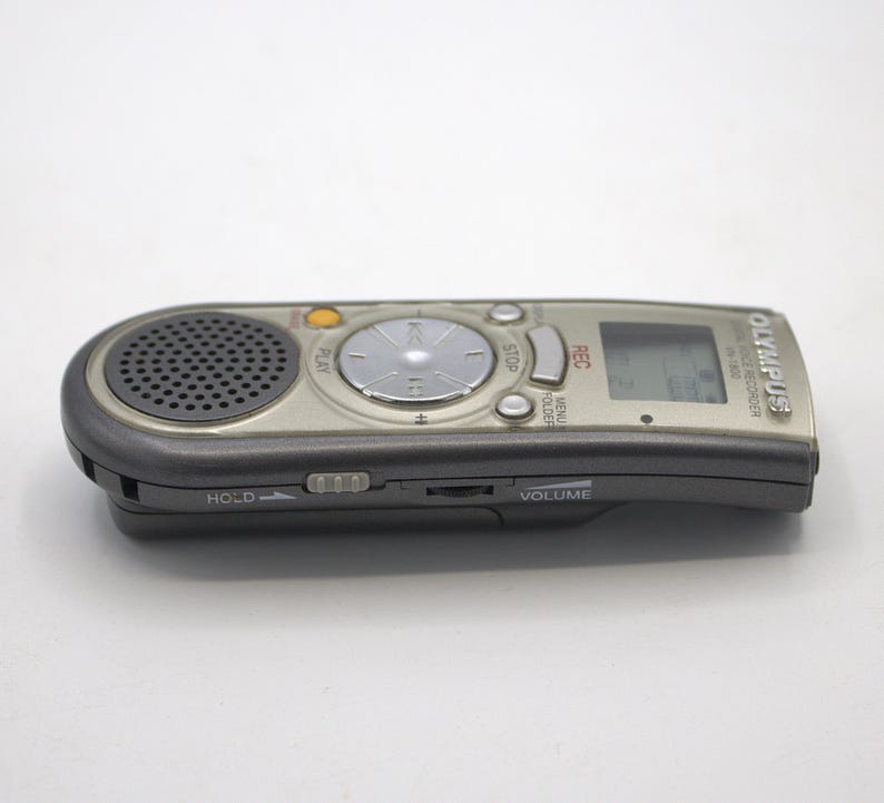 May include: A silver and black Olympus digital voice recorder with a built-in microphone, a small LCD screen, and buttons for play, stop, rec, menu, folder, and volume.