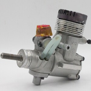 May include: A silver model airplane engine with a black and silver cylinder head, a red and yellow fuel tank, and a white fuel line. The engine has the text "YS 60 FB" printed on the side.