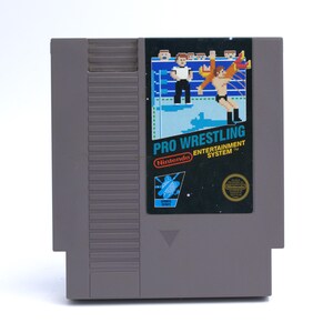 May include: A gray Nintendo Entertainment System game cartridge for "Pro Wrestling." The label features pixelated wrestlers in a ring, with the game title and Nintendo logo. The cartridge is rectangular with a beveled edge.