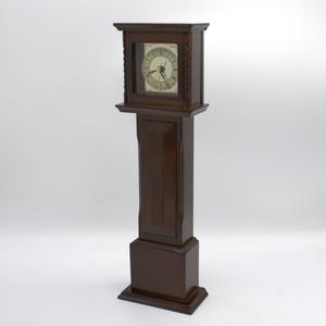 May include: A dark brown grandfather clock with a square clock face. The clock face has black hands and Roman numerals. The clock is made of wood and has a rectangular base. The clock is approximately 60 inches tall.