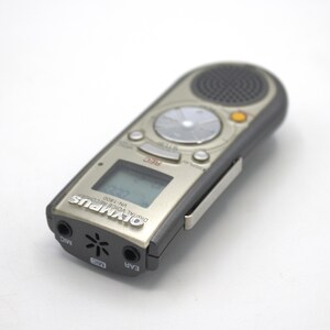 May include: A silver Olympus VN-1800 digital voice recorder with a black clip. The recorder has a small LCD screen, a record button, and a speaker.