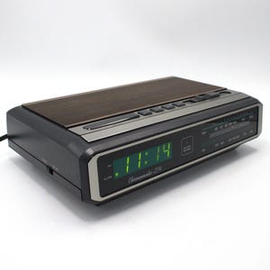 May include: A vintage black and silver digital alarm clock with a brown top. The clock displays the time as 11:14 in green digits. The clock has an AM/FM radio and the text "Chronomatic 274" is visible.