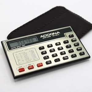 May include: A silver and black Accona Mini Card EC-821A calculator with a black leather case. The calculator displays the number 956480 on its screen. It has red and black buttons and a conversion table.