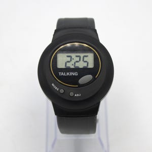 May include: Black talking watch with a digital display showing the time 2:25. The watch has a black strap and a round face with the word "TALKING" below the time. The watch has "MODE" and "ADJ" buttons.
