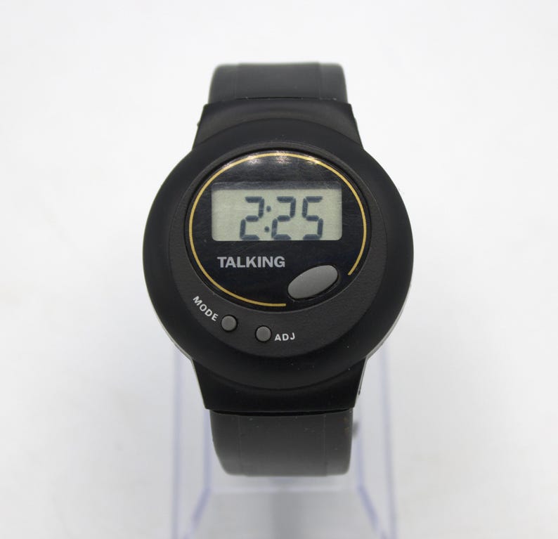May include: Black talking watch with a digital display showing the time 2:25. The watch has a black strap and a round face with the word "TALKING" below the time. The watch has "MODE" and "ADJ" buttons.